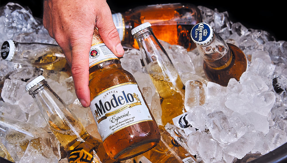 : A hand reaches for a bottle of Corona Extra in a bucket full of crushed ice (Photo: James Kern on Unsplash)