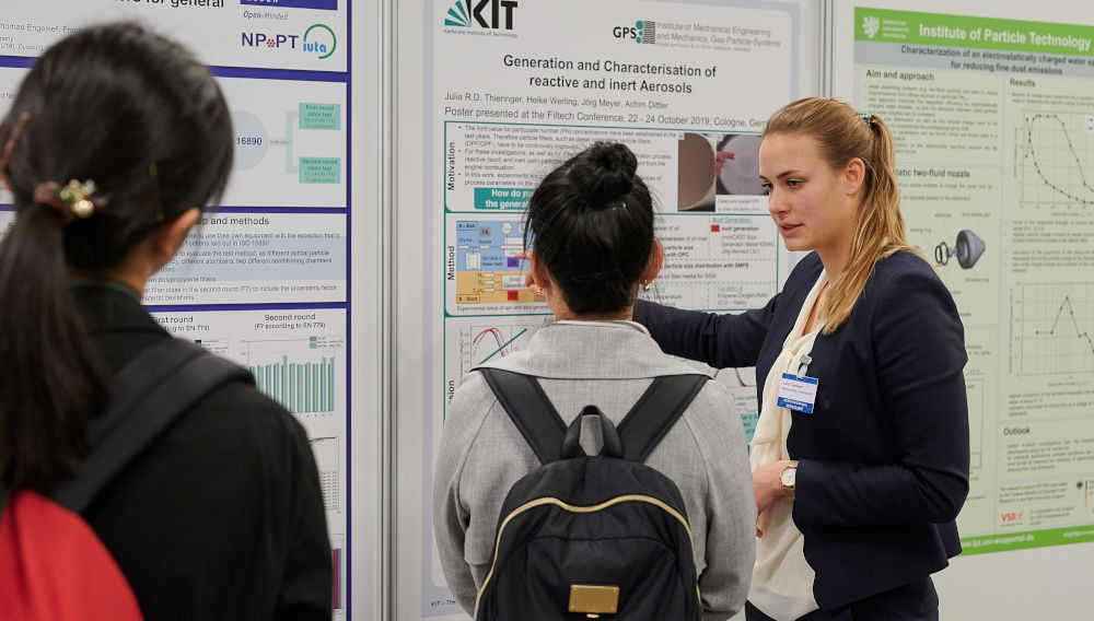 Three people during a scientific discussion in front of info posters at the Filtech conference area (Source: Filtech Exhibitions Germany)