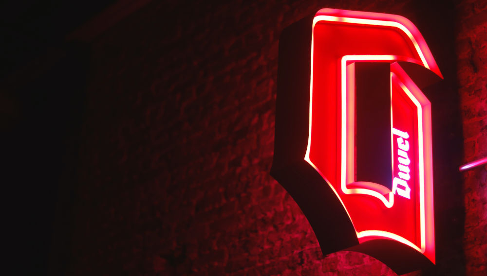 Red neon “Duvel” sign on a wall in the dark (Photo by Call me Fred on Unsplash)
