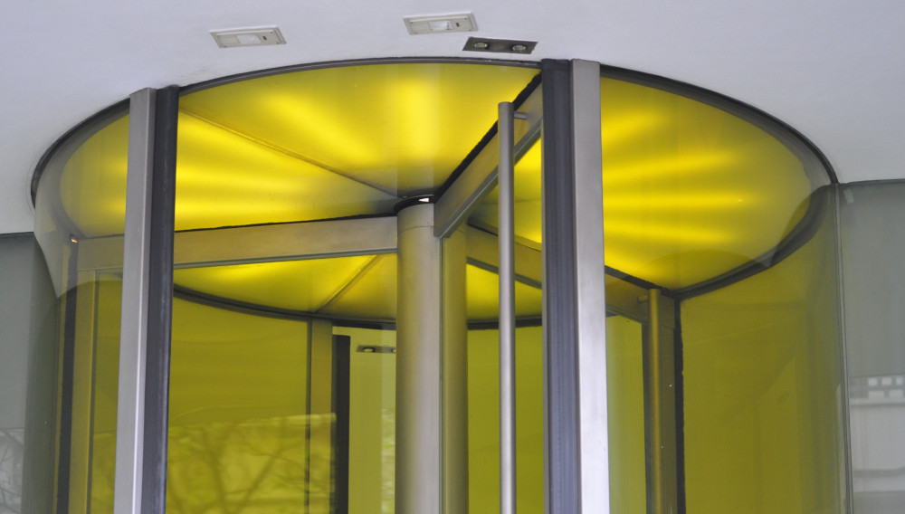 Modern revolving glass door with yellow light (Photo: therealcicero on Pixabay)