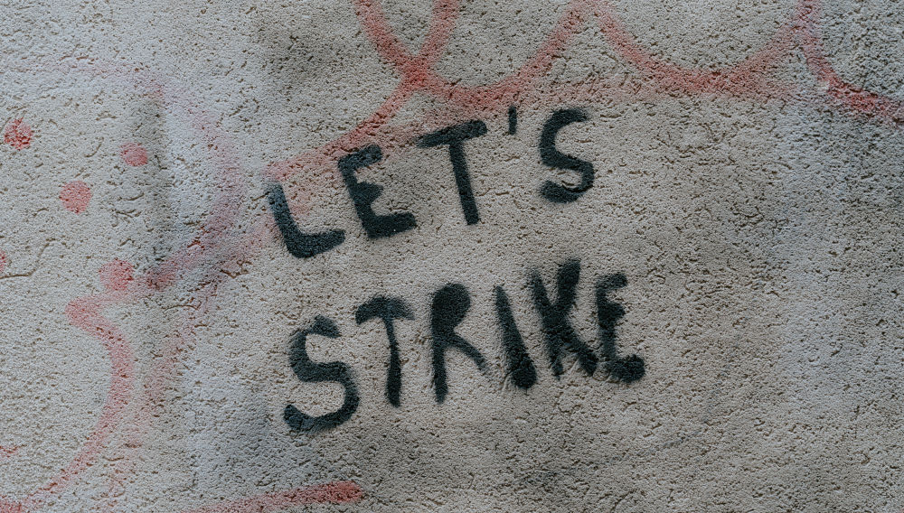 Graffiti saying Let's strike (Photo: Claudio Schwarz on Unsplash)