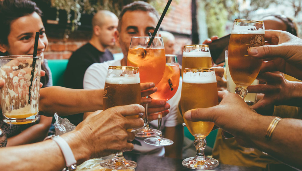 Personen an einem Tisch im Restaurant stoßen mit Biergläsern an (Fred Moon auf Unsplash)