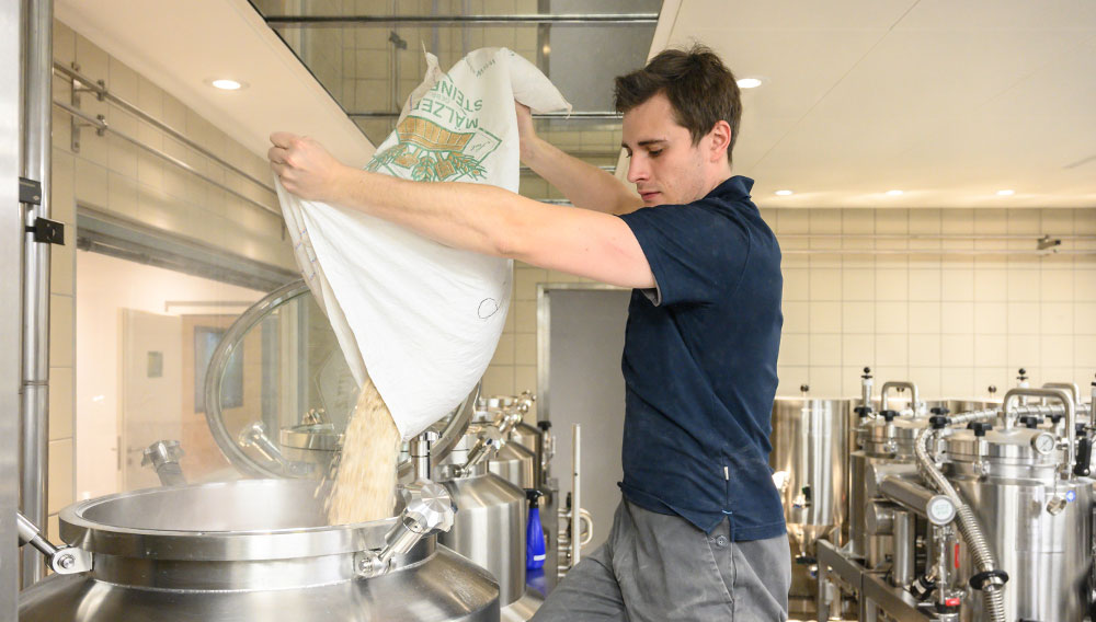 Brauer schüttet Hopfenpellets in einen Sudkessel (Foto: BarthHaas)