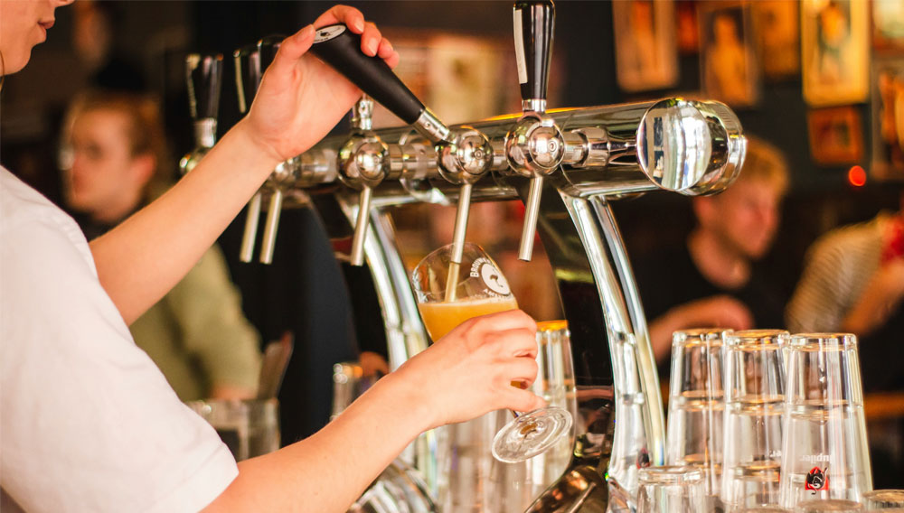 Eine Person zapft Bier in ein Glas (Foto: Louis Hansel auf Unsplash)