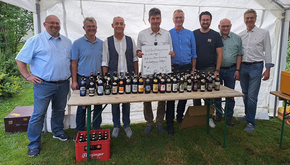Martin Schubert und Gratulanten vor einem Tisch mit Bierflaschen