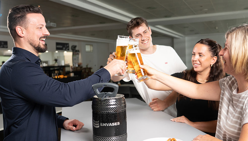 Personen stoßen mit Biergläsern an, im Vordergrund das 5-Liter-Fass von Envases Personen stoßen mit Biergläsern an, im Vordergrund das 5-Liter-Fass von Envases