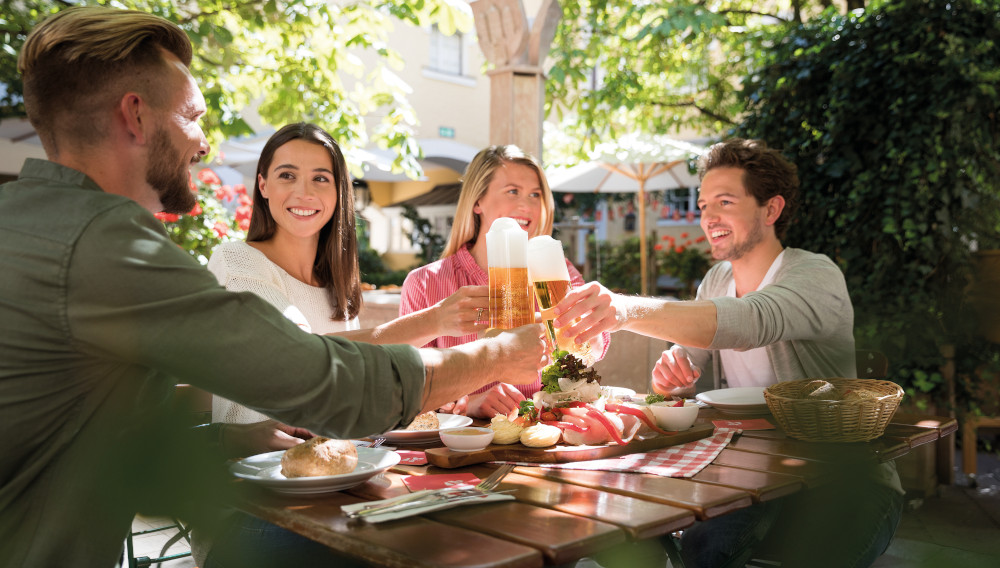 Vier Personen stoßen in einem Biergarten mit Biergläsern an (Foto: Bazzoka)