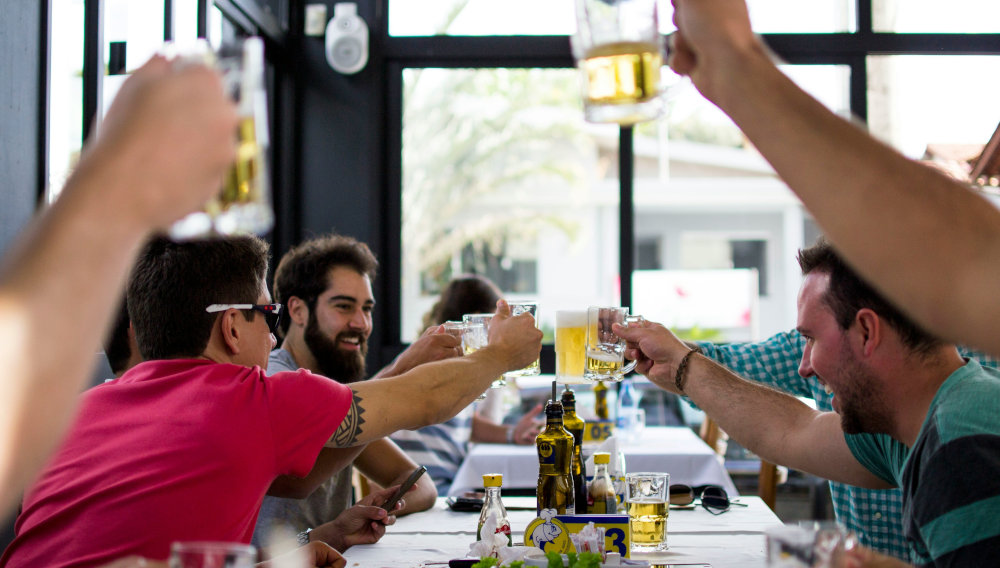 Menschen in einem Restaurant prosten sich mit Biergläsern zu (Foto: Fabio Alves auf Unsplash)