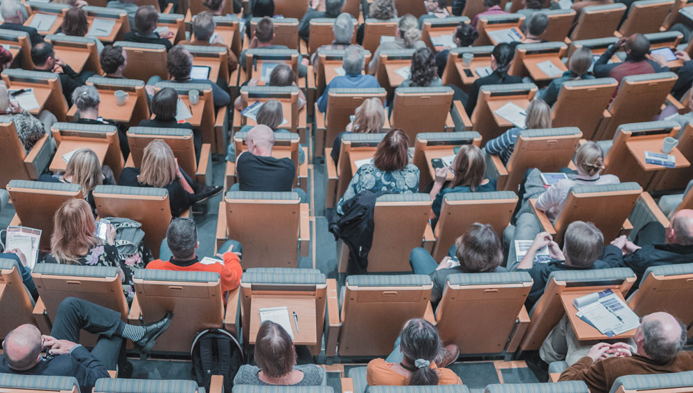 Blick von oben auf die besetzten Sessel in einem Auditorium (Bild: Mikael Kristenson auf Unsplash)